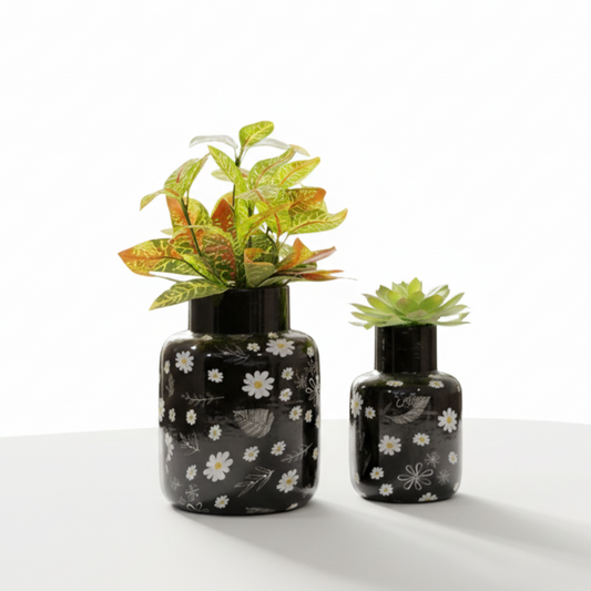 Two black vases with floral patterns, one containing a plant, on a white background