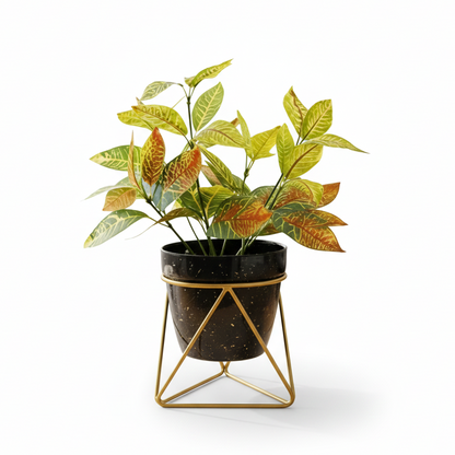 Artificial plant in a black pot with gold geometric stand on a white background
