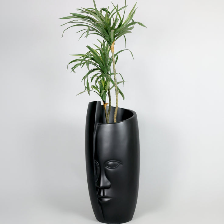 Black face-shaped planter with a plant on a white background