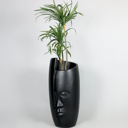 Black face-shaped planter with a plant on a white background