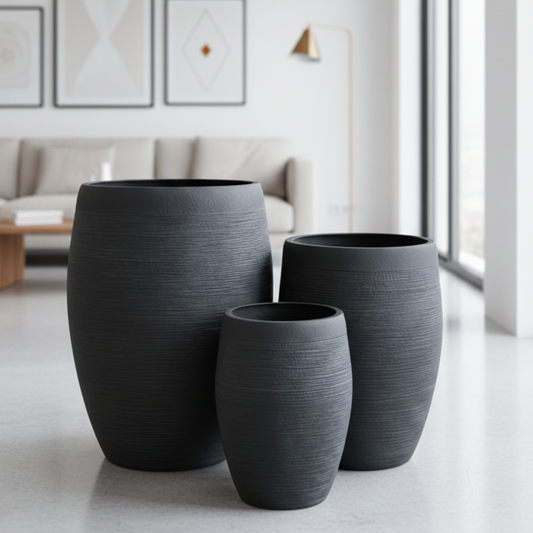 Three dark gray textured planters on a light wooden floor with a modern living room in the background.