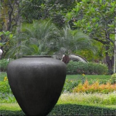 Large black vase in a garden setting with greenery and flowers.