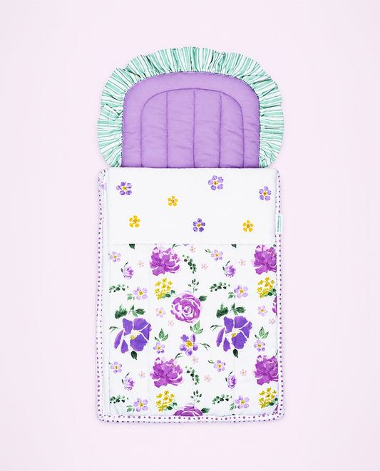 A baby sleeping bag or pouch with a purple floral print on the main body, a white upper section with small yellow and purple flowers, a light green and white fringed neck cover, and a purple padded insert at the top, shown on a pale pink background.