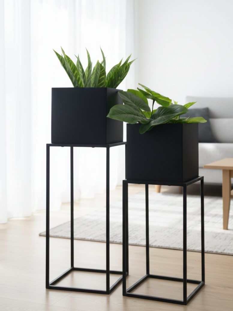 Two black planters with green plants on stands in a room.