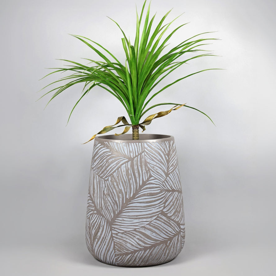 Cylindrical ceramic planter with leaf pattern containing a green plant on a light gray background